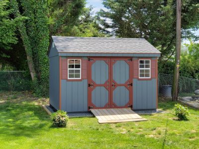 Blue Cottage Series Shed with dark red trim, double doors, 2 white windows with dark red shutters, a ramp, and light gray asphalt roofing.